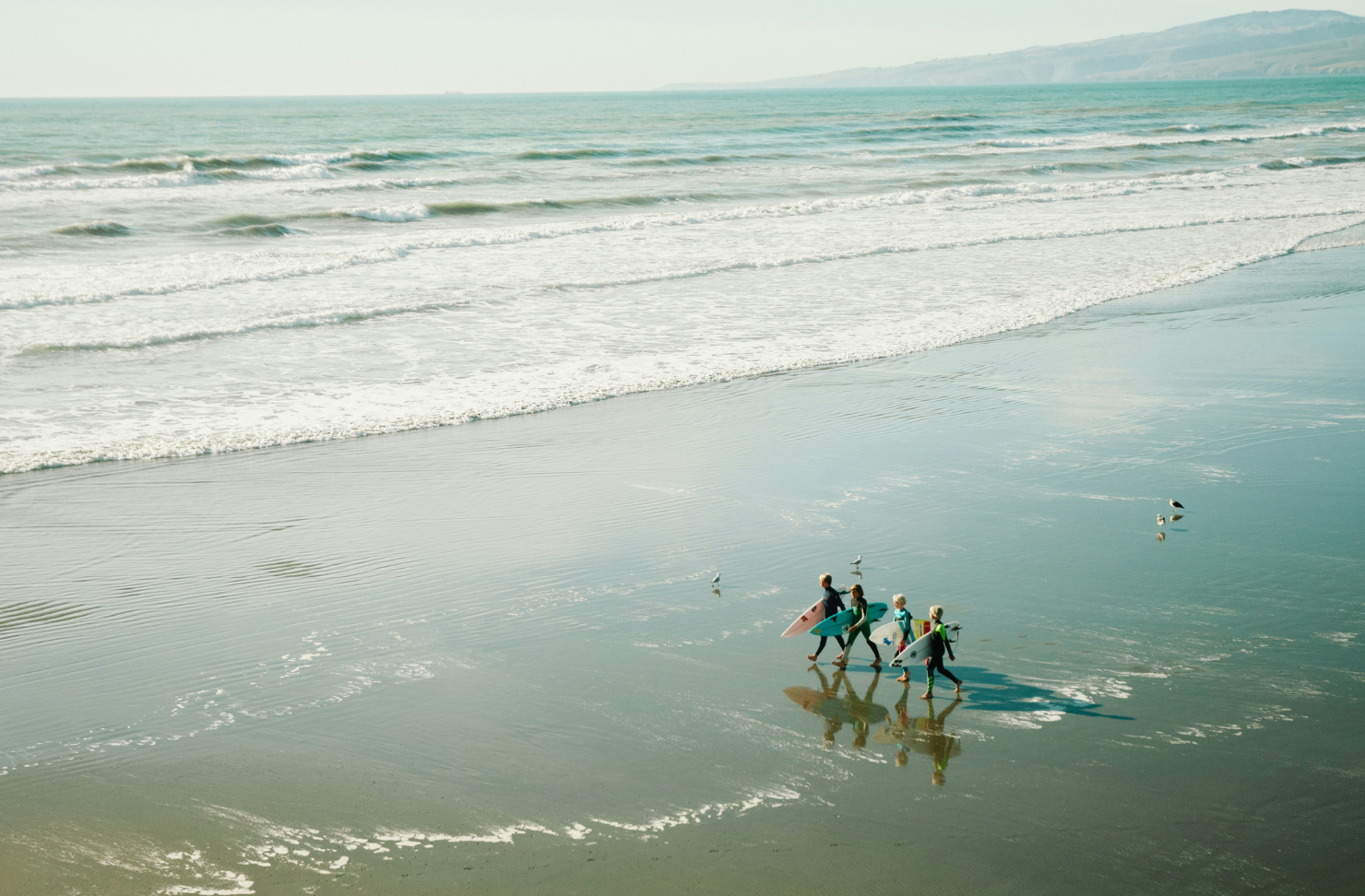 Kids walk out across Sarborough Beach in Sumner to go surfing.